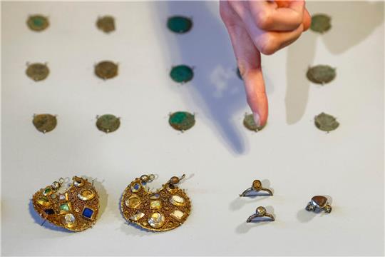 Eine Mitarbeiterin des Archäologischen Landesamtes Schleswig-Holstein deutet mit dem Finger auf zwei Ohranhänger. Mitarbeiter des Landesamtes hatten mit Hilfe von Detektoren den Schmuck aus der Zeit um 1100 gefunden. Laut Landesamt wurde der Schmuck vermutlich vor rund 800 Jahren von einem Reisenden versteckt. Foto: Frank Molter/dpa