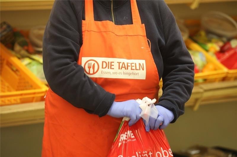Eine Mitarbeiterin mit Latexhandschuhen verpackt Lebensmittel für Bedürftige in der Tafel. Foto: Bodo Schackow/dpa-Zentralbild/dpa