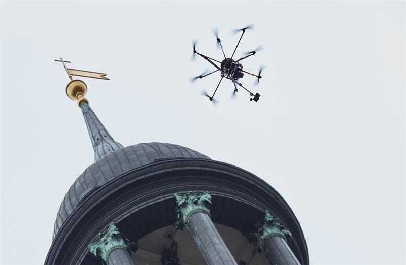 Eine Octocopter-Drohne mit Kameratechnik fliegt neben dem Kirchturm des Hamburger Michel . So nah dürfen Drohnen vielen anderen Gebäuden gar nicht kommen. Foto: Georg Wendt/dpa