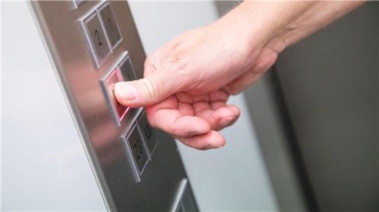 Eine Person drückt einen Knopf in einem Aufzug.