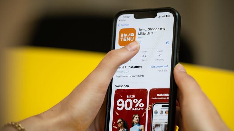 Eine Person hält ein Telefon mit der App Temu in den Händen.