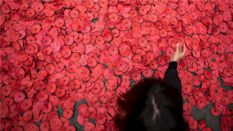 Eine Person hebt eine Papiermohnblume auf, die während einer Kundgebung gegen den Gaza-Krieg vor dem spanischen Außenministerium in Madrid auf dem Boden liegt. 