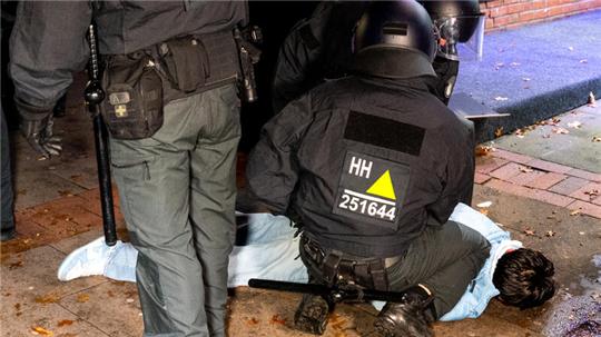 Eine Person liegt während Ausschreitungen von der Polizei fixiert auf dem Boden.