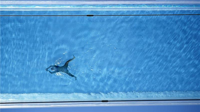 Eine Person schwimmt im Sky Pool, einem transparenten Schwimmbecken, das 35 Meter über dem Boden zwischen zwei Wohngebäuden in London aufgehängt ist, 