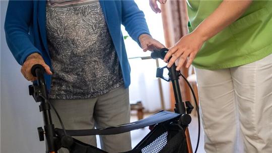 Eine Pflegefachkraft hilft einer Bewohnerin in einem Seniorenheim mit ihrem Rollator.