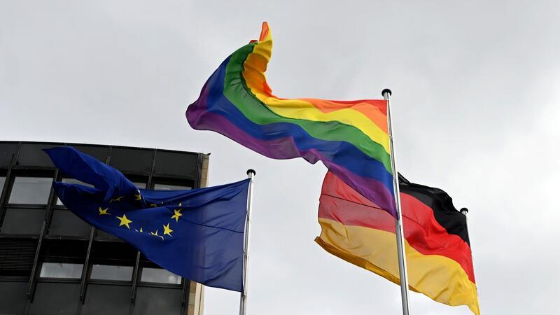 Eine Regenbogenflagge weht neben einer Deutschlandflagge und einer Europaflagge.