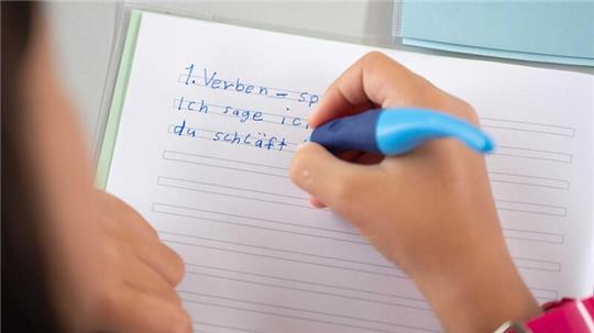 Eine Schülerin einer Grundschule soll konjugiert Verben in ihr Heft schreiben.