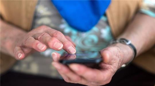 Eine Seniorin tippt auf ihrem Smartphone.