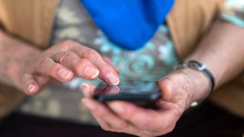 Eine Seniorin tippt auf ihrem Smartphone. Kriminelle wollen sich mit dem sogenannten Enkeltrick Geld ergaunern.