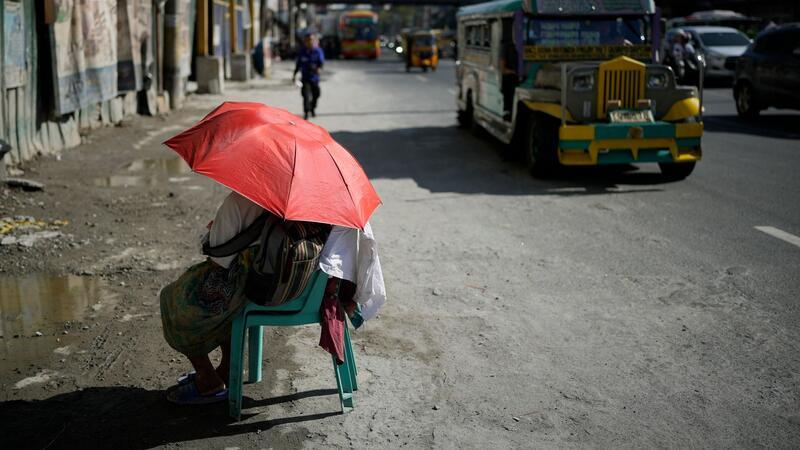 Eine Straßenverkäuferin schützt sich in Manila mit einem Regenschirm vor der Sonne.