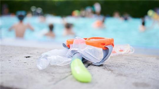 Eine Taucherbrille und Schnorchel liegen in einem Schwimmbad am Beckenrand.