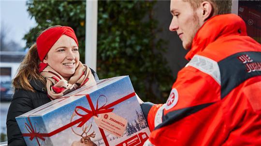 Eine Unterstützerin gibt ein Weihnachtstrucker-Paket bei einem ehrenamtlichen Helfer der Johanniter ab.