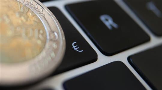 Eine Zwei-Euro-Münze liegt auf der Tastatur eines Laptops neben einem Eurozeichen. Die EBZ hebt die Zinsen vorerst nicht weiter an. (Symbolbild)