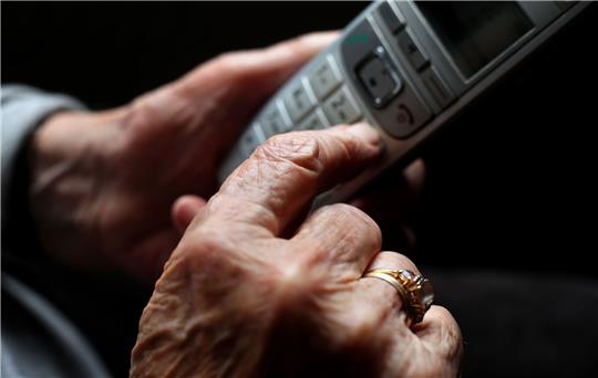 Eine ältere Frau tippt auf einem schnurlosen Festnetztelefon.