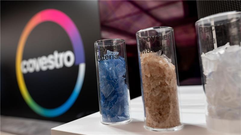 Eine deutsche Firma wird arabisch: Das Logo des Spezialchemie-Konzerns in einem Firmen-Showroom, davor Gläser mit Covestro-Materialien. 