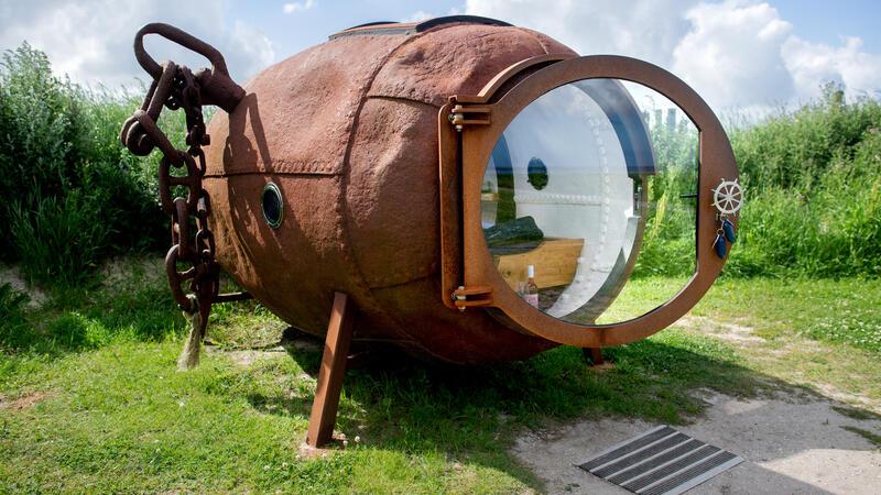 Schlafstrandkorb, Schiff oder Leuchtturm: Kurios Übernachten an Nordsee und Elbe Eine ehemalige Ankerboje, in die ein Bett und eine Glastür sowie mehrere Fenster eingebaut wurden, steht in den Dünen an der Nordseeküste.