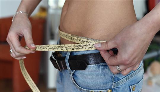 Eine junge Frau mit einem Zentimetermaß um den Bauch. Viele Mädchen haben während der Pandemie eine Essstörung entwickelt. Foto: Jens Kalaene/dpa-Zentralbild/dpa