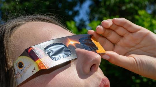 Eine junge Frau schaut durch eine Sonnenfinsternisbrille und betrachtet die Mittagssonne.