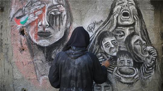 Eine palästinensische Künstlerin bemalt mit Kohle die Wände einer Schule in Deir al-Balah im Zentrum des Gazastreifens, in die sie umgesiedelt wurde.