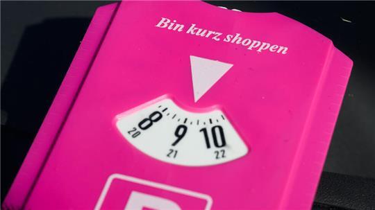 Eine pinke Parkscheibe mit Aufschrift „Bin kurz shoppen“ liegt in einem Auto in der Innenstadt.