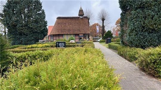 Die Friedhofskapelle Hammah hat ein Reetdach und ein kleines Glockentürmchen. Ein gepflastertert Weg führt zur Kapelle. Der Weg ist von Hecken gesäumt, einige sind gestutzt, andere nicht. 