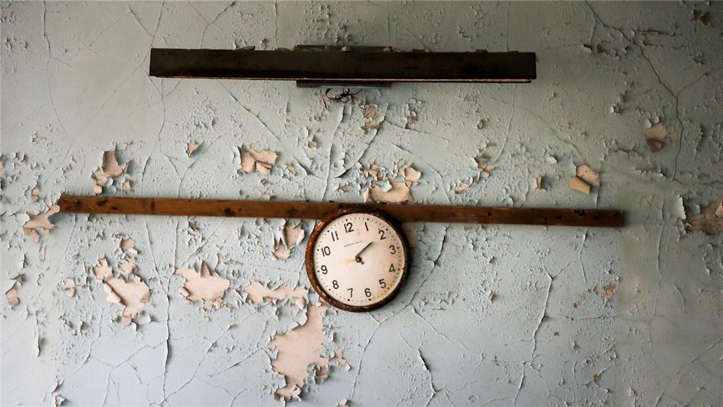 Eine zerbrochene Uhr hängt an einer Wand in einer Schule in der verlassenen Stad...