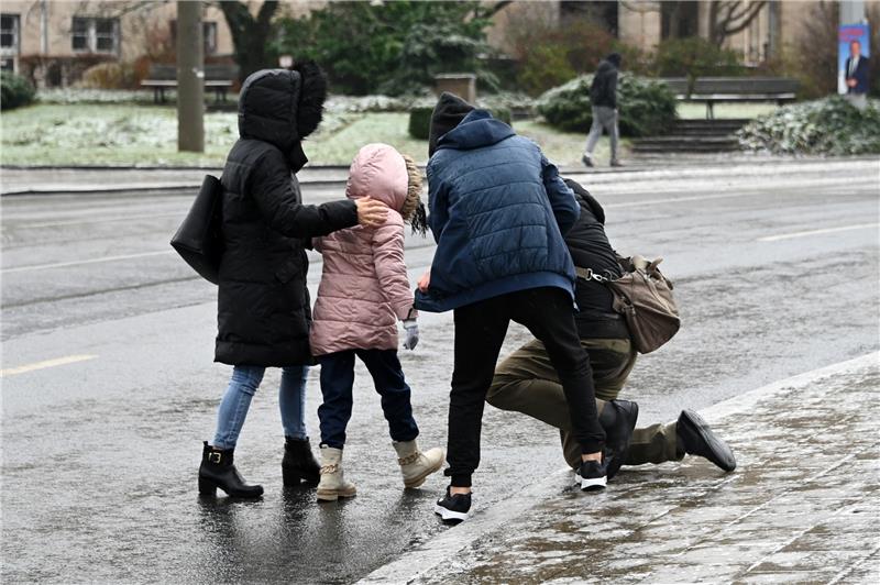 Einem Mann, der bei Eisglätte vom Gehweg auf die Straße gestürzt ist, wird aufgeholfen.  Symbolbild: Uwe Zucchi/dpa