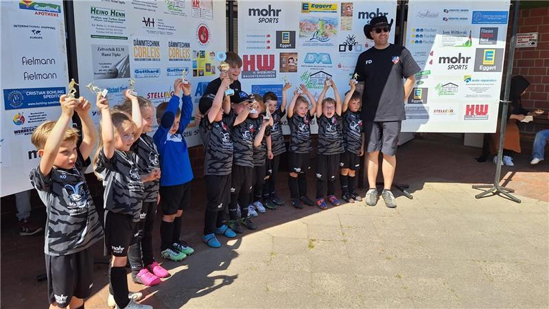 Eine Kinder-Fußballmannschaft hebt ihre Pokale nach oben und jubelt.