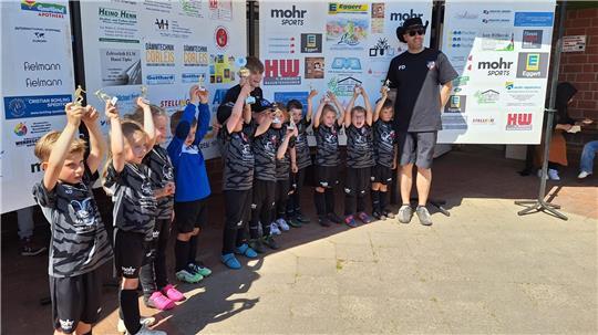 Eine Kinder-Fußballmannschaft hebt ihre Pokale nach oben und jubelt.