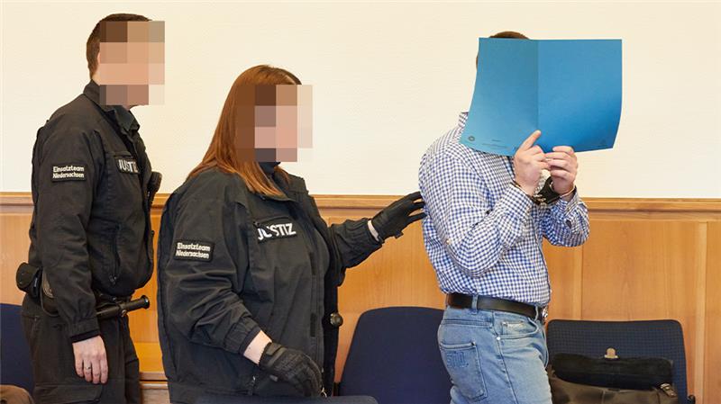 Einer der beiden Angeklagten (mit blauer Mappe vor dem Gesicht) wird vor Beginn des Prozesses am Landgericht Stade in den Gerichtssaal gebracht. Foto: Georg Wendt/dpa