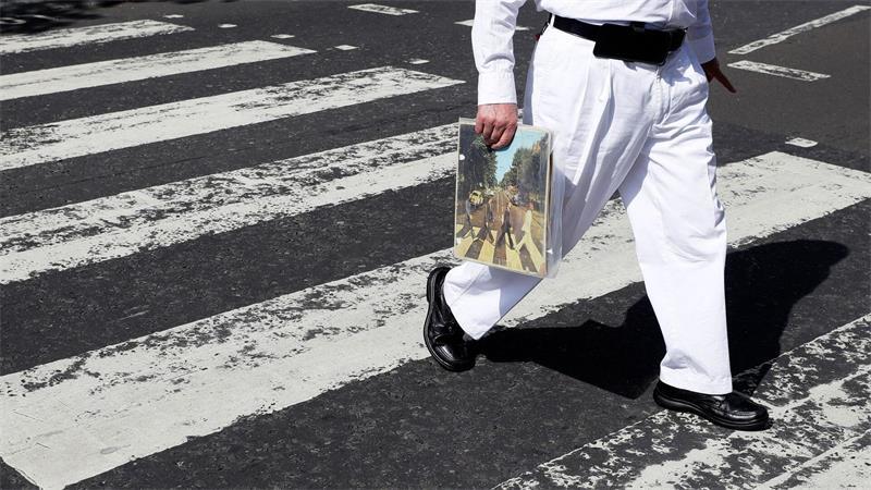 75 Jahre Zebrastreifen: Von der High Street in die Popkultur Einer der berühmtesten Zebrastreifen der Welt: Ein Fan trägt eine Ausgabe des Beatles-Albums „Abbey Road“, als er die Abbey Road überquert. (Archivfoto)