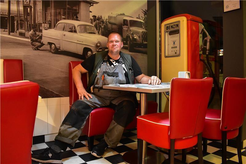 43 Jahre, „Schießereien“ und ein Mercedes: Bernd ist in Hedendorf Kult Henning in Arbeitslatzhose sitzt am Tisch im Völksen Tankshop. Auf dem Tisch vor ihm liegt eine Zeitung.