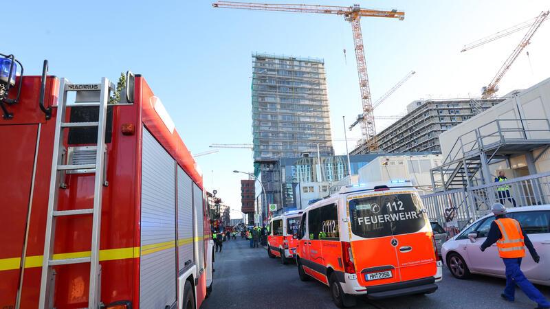 Baugerüst eingekracht: Vier tote Bulgaren in Hamburg – Schwierige Bergung Einsatzfahrzeuge der Feuerwehr stehen vor einem eingerüsteten Hochhaus.