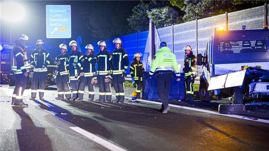 Einsatzkräfte der Feuerwehr stehen in der Nacht neben dem Baustellenfahrzeug in einer Reihe, um für vorbeifahrende Autofahrer einen Sichtschutz zu bilden.
