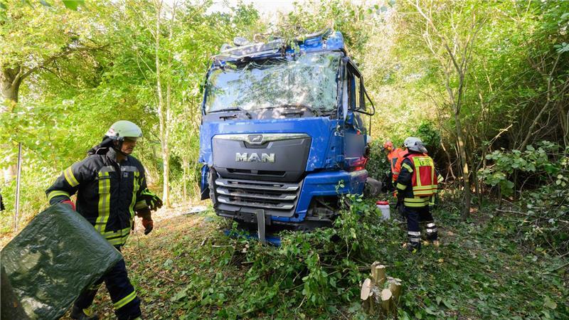 Einsatzkräfte der Feuerwehr stehen neben dem verunfallten Lkw an der Bundesstraße B3.