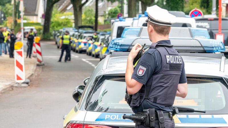 Massiver Polizeieinsatz in Hamburger Schule – Anschlags-E-Mails verschickt Einsatzkräfte der Polizei stehen in einer gesperrten Straße vor einer Stadtteilschule.