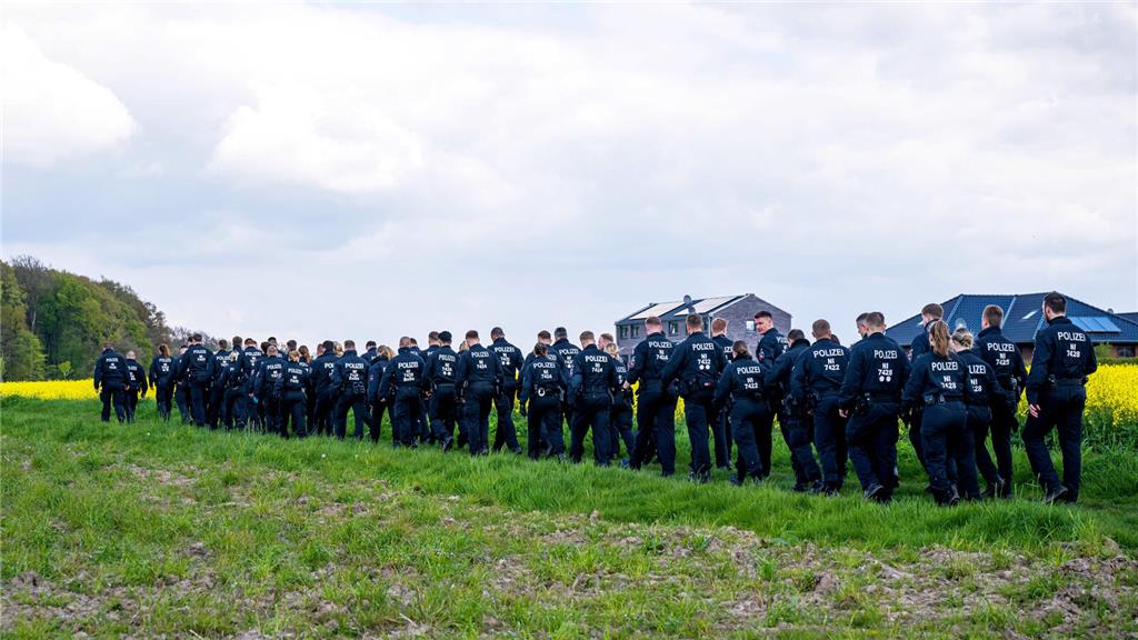Einsatzkräfte laufen über einen Feldweg auf den Wald zu. 
