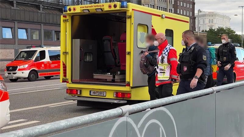 Einsatzkräfte mit Mundschutz begleiten zwei Menschen zum Rettungswagen der Feuerwehr vor dem Hauptbahnhof.