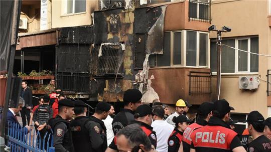 Einsatzkräfte stehen nach einem Brandausbruch vor einem teilweise verbrannten Gebäude.
