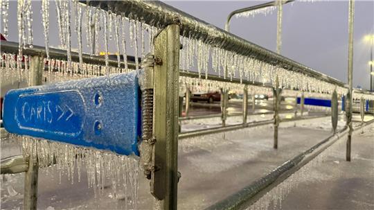 Eiszapfen hängen an einem Geländer während eines Wintersturms auf einem Parkplatz.