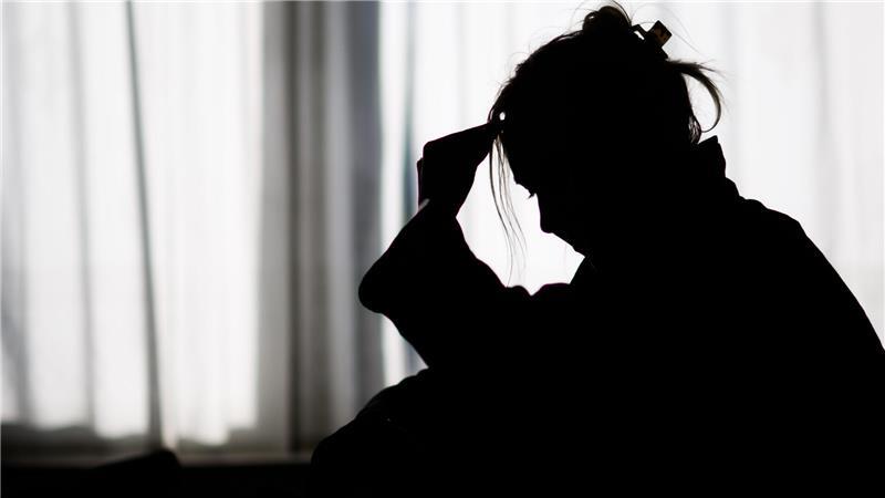  Die Silhouette einer Frau zeichnet sich vor einer hellen Fensterfront ab.