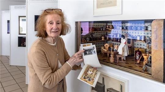 Die Betreiberin des Puppenmuseums steht vor einer Puppenküche, mit den zu diesem Objekt gehörigen Karteikarten in der Hand. 