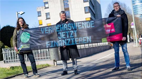 Emil Görtzen (l-r), Fridays for Future, Jürgen Schirmer, Gewerkschaft Verdi, und Patrick Steinbach, Verkehrsbetrieb BoGeStra, stehen mit einem Banner zum gemeinsamen Aktionstag vor der Verdi-Zentrale in Bochum.