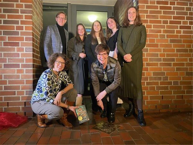 Buxtehuder Bulle: Verleihung ohne Gewinnerin Jennifer Lynn Barnes Enthüllung der BULLEvard-Plakette für Jennifer Lynn Barnes Siegertitel "The Inheritance Games" vor dem Buxtehuder Stadtarchiv mit Fachgruppenleiter Torsten Lange, Schülerinnen der IGS Buxtehude, Lehrein Franziska Sopha, Melanie Hainke vom Bullenteam und Bürgermeisterin Katja Oldenburg-Schmidt.