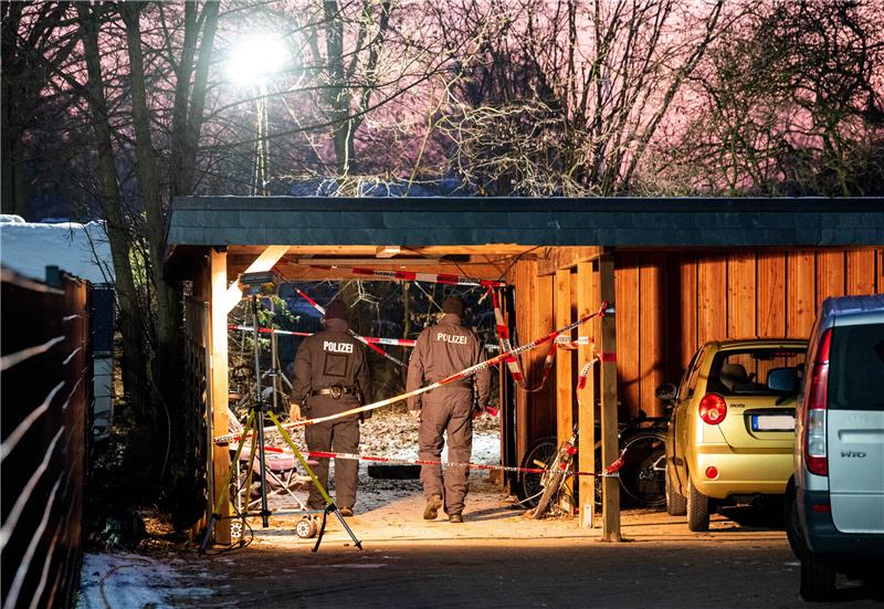 Ermittler der Polizei stehen hinter einem Mehrfamilienhaus am Zugang zu einem Garten. Foto: Daniel Bockwoldt/dpa