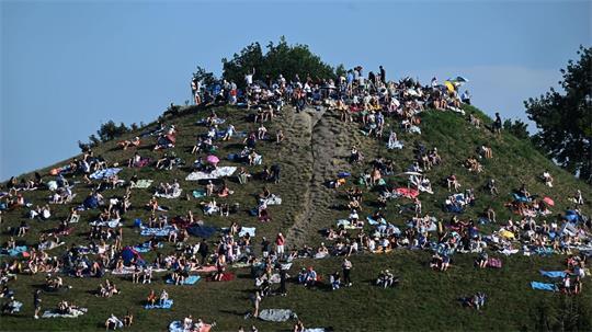 Erste Besucher bevölkern den Olympiaberg im Münchner Olympiapark, um von dort die partielle Sonnenfinsternis zu beobachten.