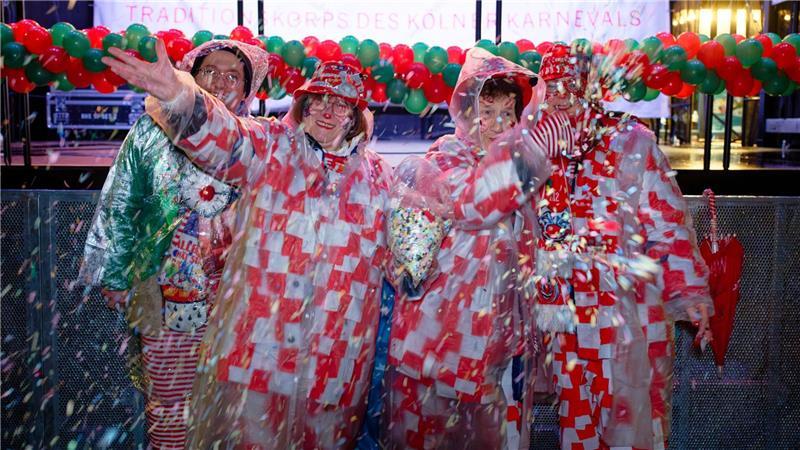 Erste Jecken warten im Regen auf dem Alter Markt an Weiberfastnacht auf den Beginn des Straßenkarnevals in Köln.