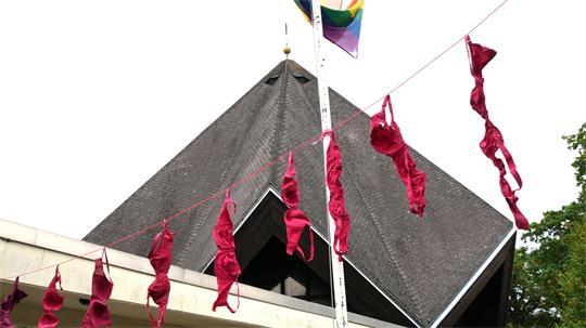 Erstmals beteiligt sich auch die katholische Kirchengemeinde am Pinktober und wirbt mit einer BH-Girlande für Brustkrebsvorsorge.