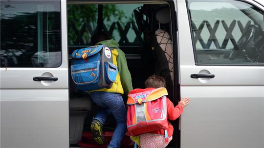 Zwei Kinder steigen in ein Auto ein.