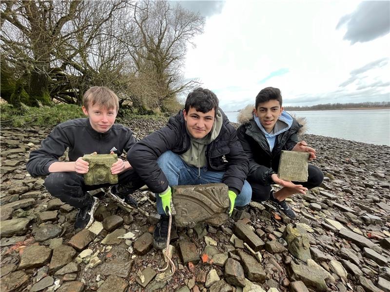 Etienne Gervais und Sharbel Assi nehmen Nelson Neves in ihre Mitte. Dieser hält ein Fragment eines jüdischen Grabsteins in Händen. Nach dem Zweiten Weltkrieg diente der Strand bei Neuenschleuse als Deponie für Hamburger Bombenschutt. Foto: 